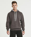 A young man stands facing forward, wearing an AWDis Just Hoods JH100 dark grey hoodie with white drawstrings and black pants. The background is plain white.