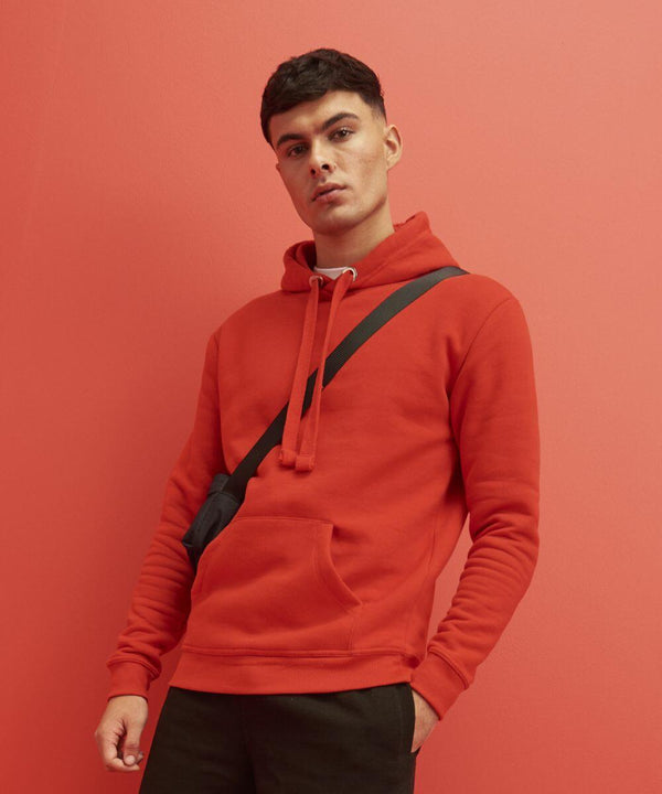 A person wearing a AWDis Just Hoods JH101 red hoodie and black crossbody bag stands against a matching red background.