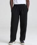 Only the lower half of a person is visible, wearing AWDis Just Hoods Signature heavyweight joggers in black, paired with black and white trainers and a white shirt, standing on a white background with hands in pockets.