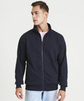 A man is wearing an AWDis Just Hoods JH147 navy zip-up jacket over a pink t-shirt. He is looking to his left and standing against a plain white background.
