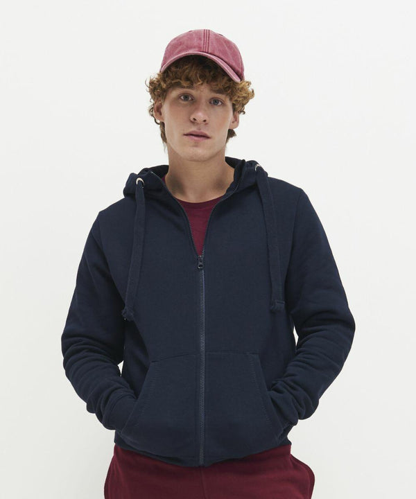 A person with curly hair wears a red cap, a navy blue AWDis Just Hoods JH150 hoodie with a zipper, and maroon pants. They are looking directly at the camera against a plain white background.