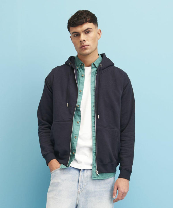 A person stands against a blue background wearing a black JH250 hoodie by AWDis Just Hoods over a green shirt and a white t-shirt, with light blue jeans.