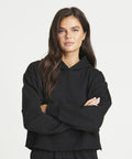 A person with long dark hair wearing a AWDis Just Hoods JH305 stands with their arms crossed against a plain white background.