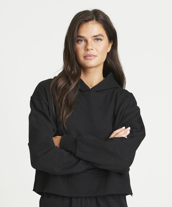 A person with long dark hair wearing a AWDis Just Hoods JH305 stands with their arms crossed against a plain white background.