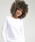 Person with curly hair smiling and wearing an AWDis Just Hoods JH30F plain white long-sleeve shirt against a neutral background.