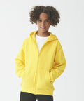 A young person with curly hair wearing an AWDis Just Hoods JH50J and black pants stands against a plain white background.