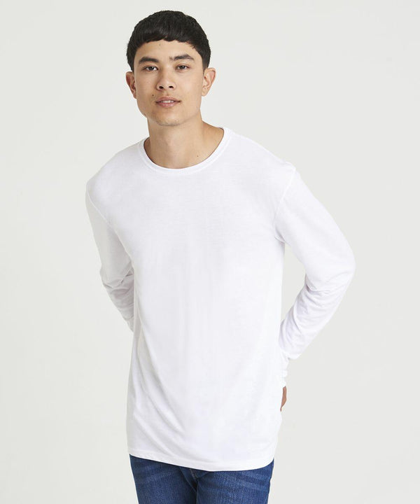 A person with short dark hair is wearing an AWDis Just T's JT002 plain white long-sleeve T-shirt and blue jeans, standing against a plain light background.