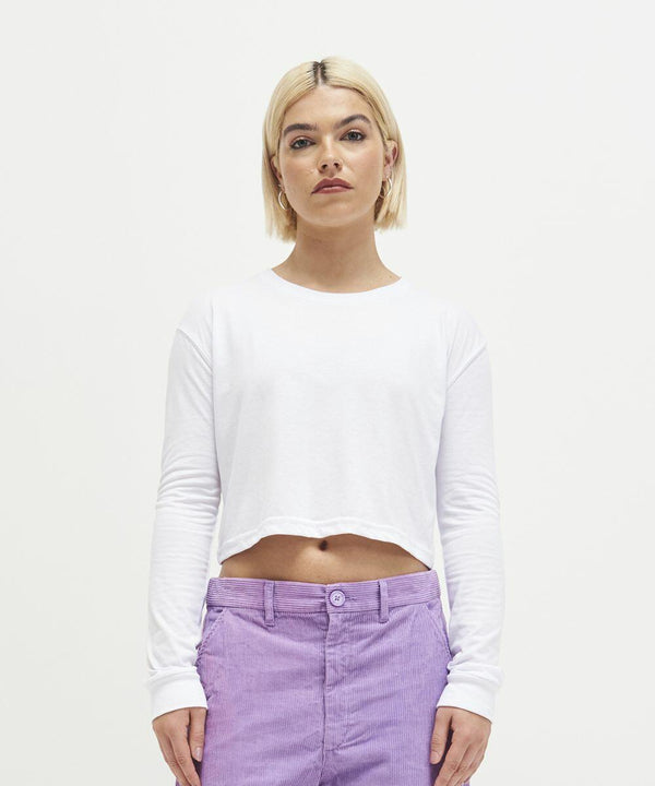 Person with short blonde hair wearing a long-sleeve white crop top and purple pants, standing against a plain white background, featuring the JT016 by AWDis Just T's.