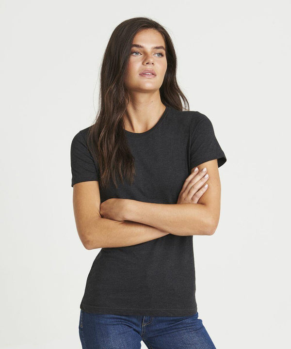 A person with long dark hair, wearing an AWDis Just T's JT01F t-shirt and blue jeans, stands with arms crossed against a white background.