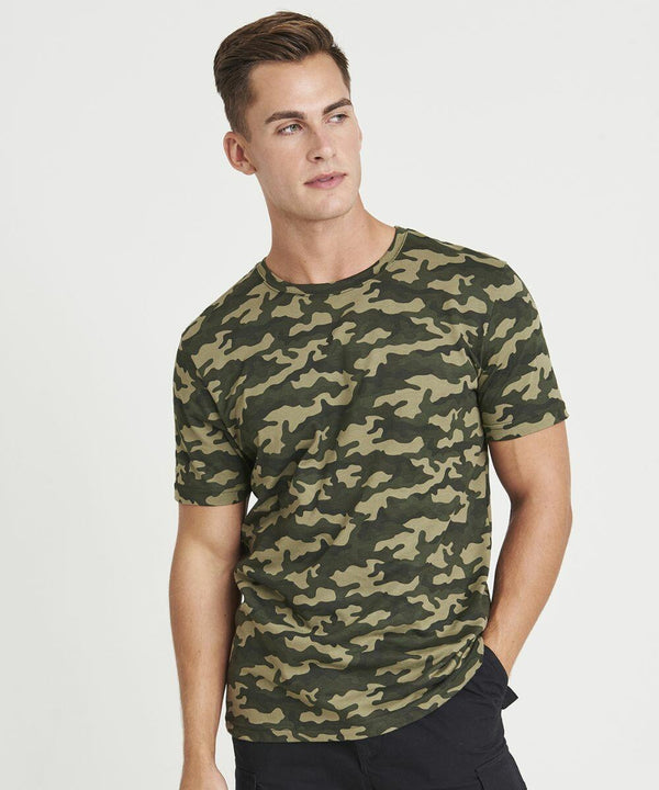 A person in a camouflage-patterned JT034 from AWDis Just T's and dark pants looks to the side against a plain white background.