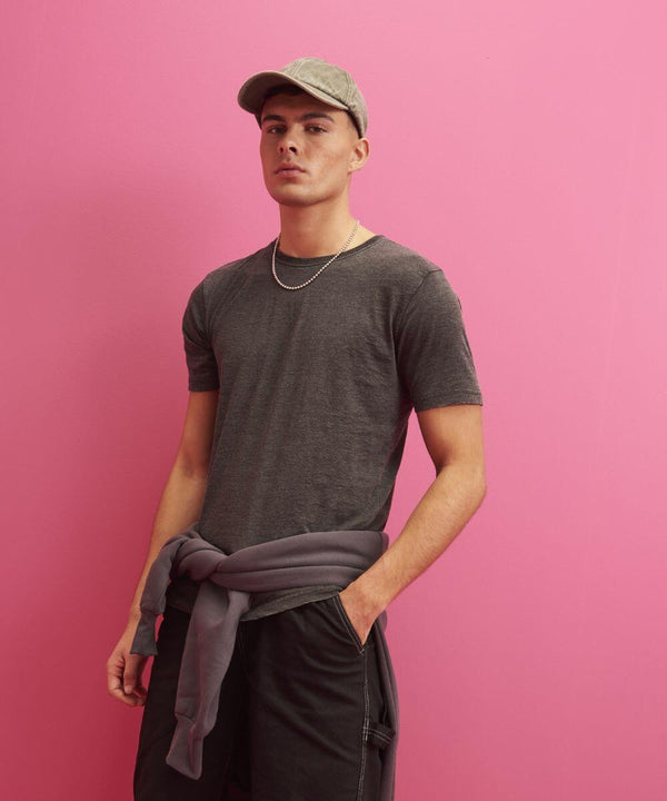 A man wearing an AWDis Just T's JT099 grey t-shirt, grey cap, and dark pants with a grey sweatshirt tied around his waist stands against a pink background.