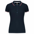 The KB251 by Kariban is a navy blue polo shirt featuring red and white stripes on the collar and sleeve edges, along with a buttoned placket.