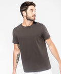 A man with short brown hair, facial hair, and a tattoo on his arm is wearing a Kariban KB356 t-shirt and looking to the side against a light background.