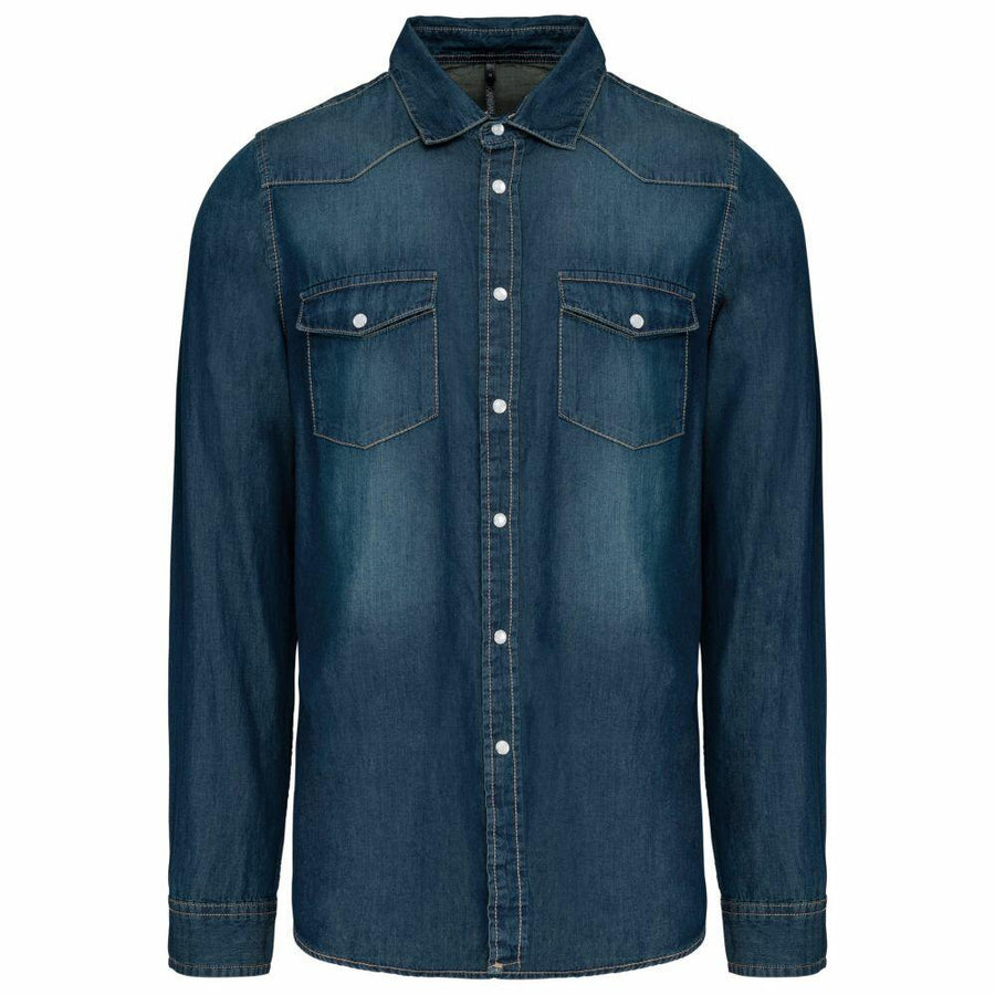 The Kariban KB519 is a dark blue denim shirt featuring long sleeves, a button front, and two chest pockets.