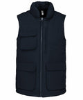 A navy blue sleeveless puffer vest with multiple front pockets and a zip-up closure, the Kariban KB615.