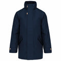 Introducing the Kariban KB677: a navy blue winter coat with a high collar and front zipper. This stylish coat features long sleeves adorned with beige button details and angled pockets on both sides, all in a sleek and minimalistic design.