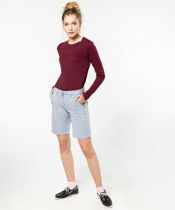 A woman wearing a maroon long-sleeve shirt, light gray shorts, white socks, and black boat shoes stands with her hands in her pockets against a plain white background, showcasing the KB753 by Kariban.