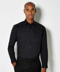 A man wearing a Kustom Kit KK104 black long-sleeve button-up shirt and black pants stands against a plain white background.