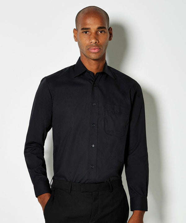 A man wearing a Kustom Kit KK104 black long-sleeve button-up shirt and black pants stands against a plain white background.