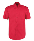 The KK109 by Kustom Kit is a red, short-sleeved button-up shirt featuring a pointed collar and a single chest pocket. The shirt is neatly pressed and showcased against a plain white background.