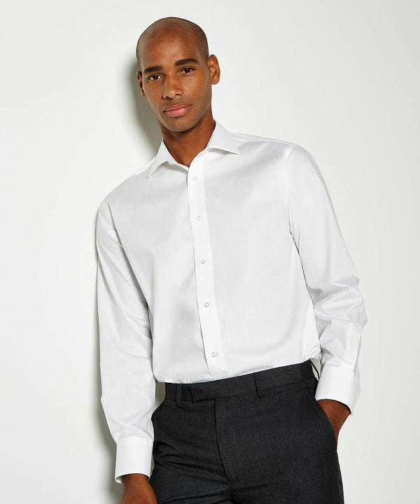A man wearing a white KK118 dress shirt by Kustom Kit and dark trousers stands against a plain background, looking towards the camera.