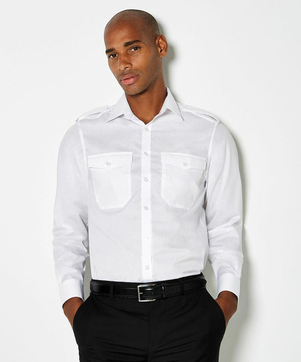 A person is standing against a plain background, wearing a white long-sleeve Kustom Kit KK134 button-up shirt with two front pockets and black pants.