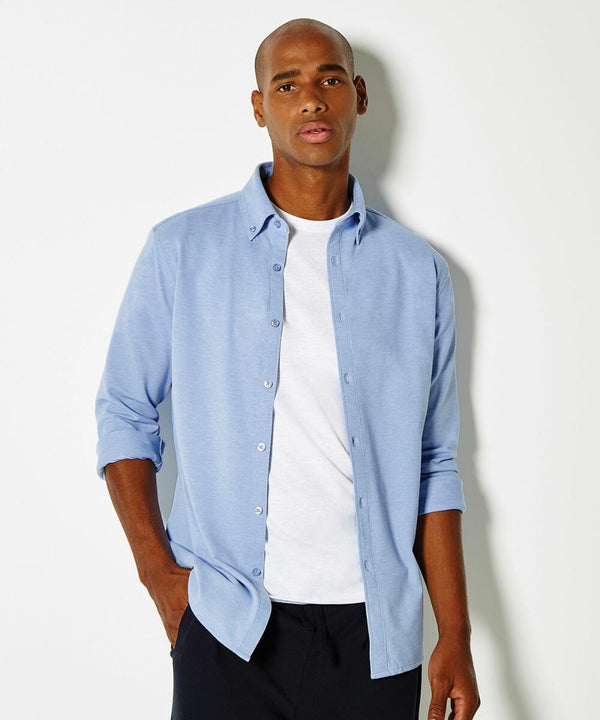 Man wearing a Kustom Kit KK143 light blue button-up shirt over a white t-shirt, with one hand in his pocket, standing against a plain background.