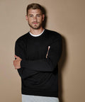 A man with short hair and a beard stands against a beige background, wearing the KK253 Kustom Kit sweater over a white shirt, with his arms crossed.
