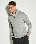 Man wearing a light gray Kustom Kit KK335 quarter-zip pullover and dark pants, looking to his left, standing against a plain white background.