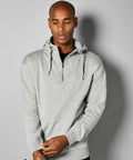 A man wearing a grey KK336 hoodie by Kustom Kit stands against a plain background, looking down with his hands clasped.