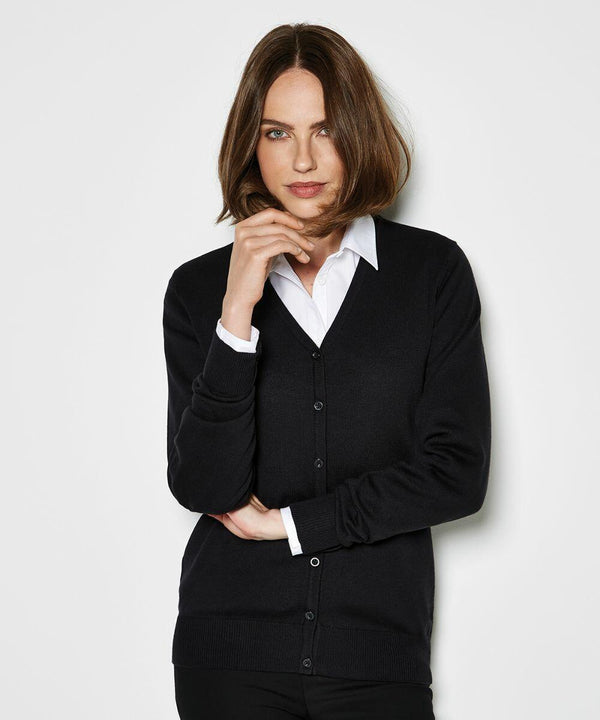 A person with shoulder-length brown hair wearing a black buttoned Kustom Kit KK354 over a white collared shirt poses against a plain backdrop.
