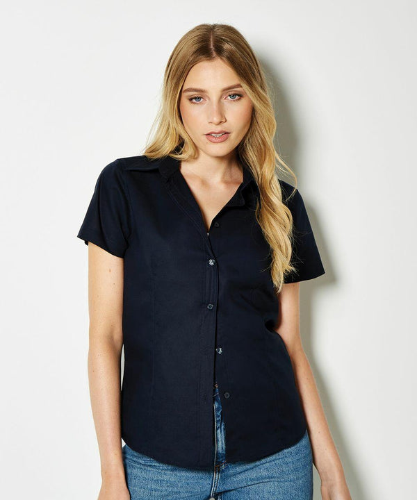 A person with long blonde hair is wearing a short-sleeved, button-up, black KK360 shirt by Kustom Kit and blue jeans, standing against a plain white background.