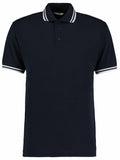 The Kustom Kit KK409 is a black polo shirt featuring short sleeves and a buttoned collar, accented with white stripes on the collar and sleeve edges.