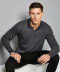 A person with short dark hair wearing a Kustom Kit KK430 and black pants is sitting against a gray background.