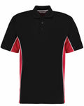 The Gamegear KK475 features a black polo shirt with red side panels and white piping, complemented by a classic collar and a three-button placket. The shirt is showcased against a white background.