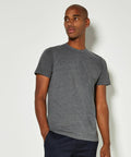 A man wearing a gray Kustom Kit KK504 t-shirt and dark pants stands against a plain white background, looking slightly to his right with one hand in his pocket.