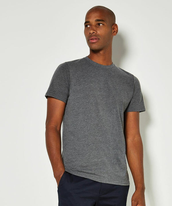 A man wearing a gray Kustom Kit KK504 t-shirt and dark pants stands against a plain white background, looking slightly to his right with one hand in his pocket.