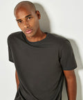 A person with a shaved head, wearing a dark t-shirt, stands against a light-colored wall, looking directly at the camera in a Kustom Kit KK530.