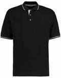 The Kustom Kit KK606 is a black polo shirt with white trim on the collar and sleeves and features a three-button placket.
