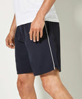 A person is wearing black Kustom Kit KK980 athletic shorts with a white stripe on the side and a white T-shirt. The image focuses on the lower half of the person's body.