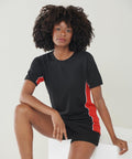 A person with curly hair wearing a black and red Finden & Hales LV240 sports outfit sits with one leg bent and the other extended, posing for the camera.