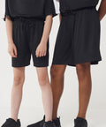 Two people stand side by side wearing Finden & Hales Kids team shorts with no pockets, black trainers, and black shirts. The image shows only their bodies from the chest down, set against a plain white background.