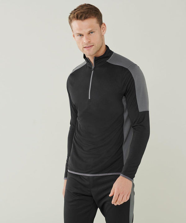A man stands facing the camera wearing a black and gray Finden & Hales LV571 long-sleeve athletic shirt with a zipper at the collar. He has short brown hair and is smiling slightly.