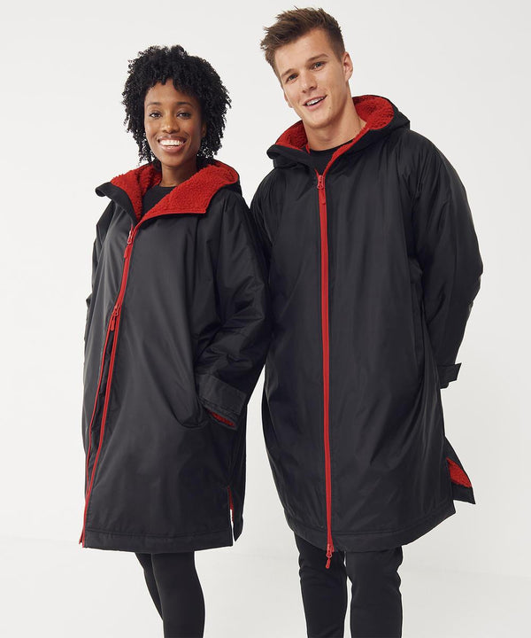 Two people stand side by side, smiling at the camera in Finden & Hales All-weather robes—long black hooded jackets with red fleece lining and red zips—against a plain white background.