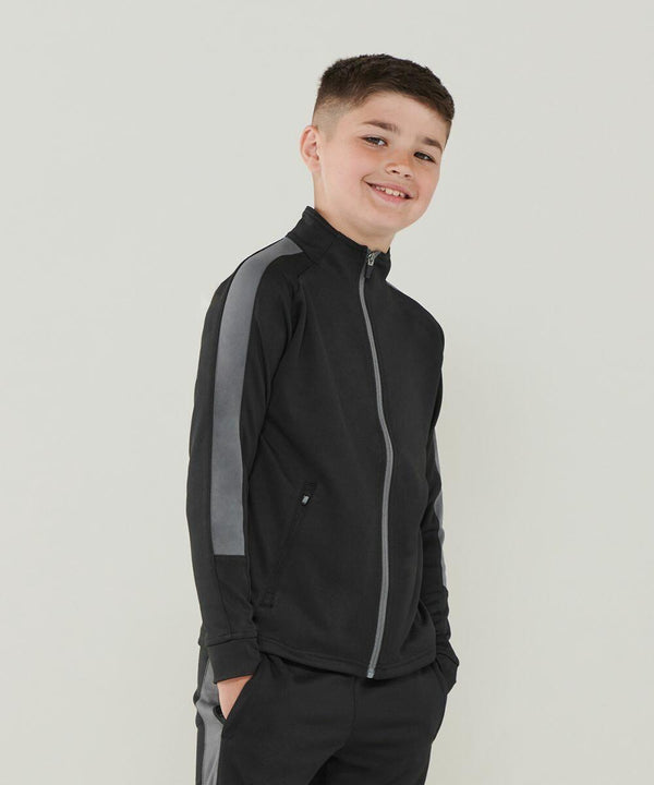 A young boy in a black and gray Finden & Hales LV873 zip-up jacket stands against a plain background, smiling with hands in his pockets.