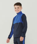 Smiling boy wearing a blue and navy Finden & Hales LV875 zip-up sports jacket with matching pants stands against a plain background.