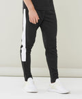 Man wearing black Finden & Hales LV881 athletic track pants with white side stripes and white athletic shoes against a plain background.