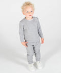 A young child with curly blonde hair stands wearing a Larkwood LW06T grey long-sleeve shirt, matching grey sweatpants, and white sneakers, looking slightly off-camera against a plain background.
