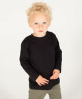 A young child with curly blond hair and blue eyes is wearing a black Larkwood LW21T long-sleeved shirt and green pants, standing against a plain white background.