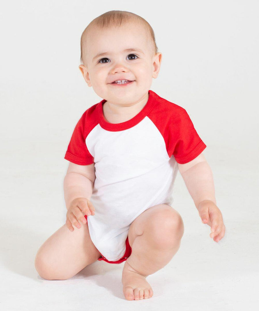 A smiling baby wearing a Larkwood LW502 onesie with red sleeves is sitting on the floor, looking slightly upward.